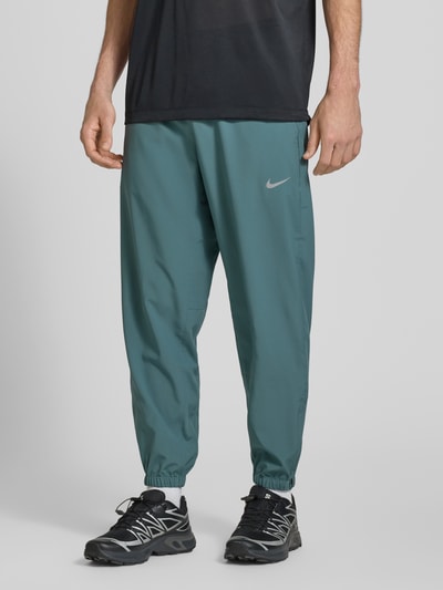 Männermodel trägt Form Pants mit Logo-Print und Eingrifftaschen von NIKE TRAINING, körpernah, elastisch, blaugrün, Ganzkörperansicht von vorne.