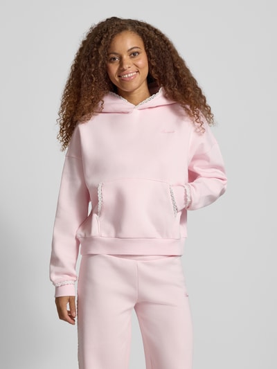 Frauenmodel trägt Hoodie mit Häkelspitzenbesatz von REVIEW in Rosa, lockere Passform, Baumwollmischung, Logo-Print, Kängurutasche, gerippte Abschlüsse, Ganzkörperansicht von vorne.