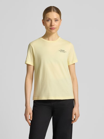 Modelka nosi T-Shirt mit Label-Print und Rundhalsausschnitt od Gant z bawełny, krój regular fit, nadruk z logo, okrągły dekolt, długość tyłu w rozmiarze S: 57 cm, jasny żółty, prosty fason, gładka tekstura, pełen widok z przodu.