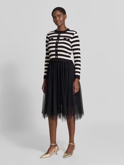 Modelka nosi Knielanges Kleid aus Viskose-Mix im 2-in-1-Look von Apricot, Mieszanka wiskozy, linia a, długość do kolan, efekt 2 w 1, okrągły dekolt, listwa guzikowa, długość tyłu w rozmiarze S: 107 cm, szerokość w rozmiarze S: 39 cm, długość rękawów w rozmiarze S: 58 cm, czarne i białe pasy, tiulowa spódnica, widoczna faktura dzianiny, Ganzkörperansicht z przodu