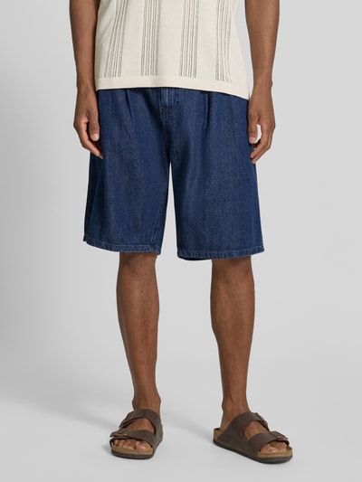 Męski model nosi Regular Fit Jeans-Bermudas aus Baumwoll-Lyocell-Mix Modell 'DENIM' von Armedangels, stylizowana na denim, 5 kieszeni, mieszanka bawełny i lyocellu, naszywka z logo, zapięcie na guzik i zamek, szlufki na pasek, widok całej sylwetki z przodu.