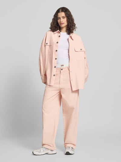 Frauenmodel trägt Oversized Hemdjacke mit Brusttaschen von Karo Kauer aus reiner Baumwolle in Hellrosa, sichtbare Knopfleiste und große Taschen, kombiniert zu weiter Hose, Ganzkörperansicht von vorne.