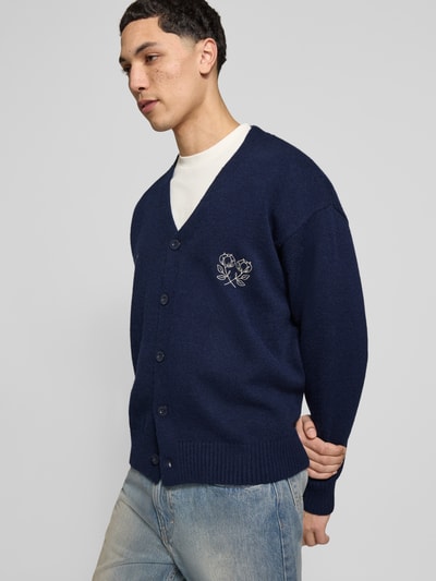 Männermodel trägt Cardigan mit Logo-Stitchings und Knopfleiste von ANOTHER COTTON LAB, Gerader-Schnitt, V-Ausschnitt, Gerippte-Abschlüsse, dunkelblau, Ganzkörperansicht von vorne.