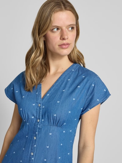 Kobieta modelka nosi Tailliertes Jeanskleid aus reiner Baumwolle Modell 'NOVA AZURE' von Only, niebieski denim, krótki rękaw, dekolt V, średniej długości, allover wzór, czysta bawełna, zapięcie na guziki, widok na górną część ciała z przodu.