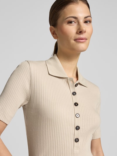 Kobiece modelka nosi Slim Fit Poloshirt aus Baumwoll-Modal-Mix von Marc O'Polo, efekt: jednolity kolor, krój slim fit, aplikacja z wyhaftowanym logo, kołnierzyk polo, zapięcie: krótka listwa guzikowa, rękaw: krótki, wykończenie materiału: prążkowana dzianina, mieszanka bawełny i modalu, jasny beż, widoczna prążkowana faktura, nahaufnahme górna część ciała