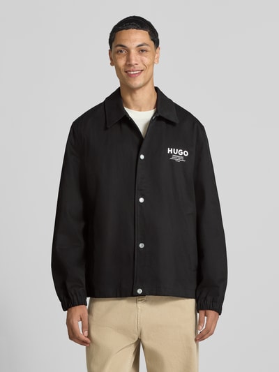 Männermodel trägt Regular Fit Bomberjacke / Blouson aus reiner Baumwolle Modell 'Biyo2631' von HUGO Blue in Schwarz, Ganzkörperansicht von vorne.