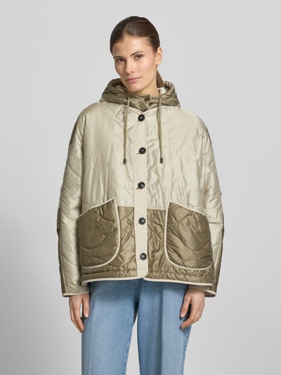 Frauenmodel trägt Steppjacke mit aufgesetzten Eingrifftaschen und Kapuze von Blonde No. 8 in Beige und Oliv, glatte Textur, Ganzkörperansicht von vorne. Gerader Schnitt, Kapuze mit Kordelzug, Knopfverschluss, verstellbarer Saum, Maße: Rückenlänge 71 cm, Schulterbreite 45 cm, Brustweite 68 cm, Ärmellänge 52 cm.