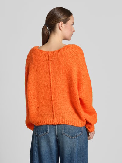 Frauenmodel trägt Oversized Strickpullover mit Mohair-Anteil von Oui in leuchtendem Orange, grobe Strickstruktur, gerippte Abschlüsse, Rückenlänge 37 cm, Ärmellänge 48 cm, Material-Mix-Optik, Ganzkörperansicht Rückansicht.