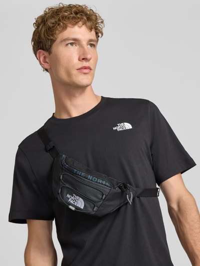 Männermodel trägt schwarze Bauchtasche mit Logo-Print Modell 'Jester' von The North Face, Reißverschluss, Oberkörperansicht von vorne.