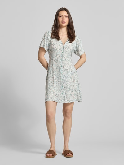 Frauenmodel trägt Minikleid aus reiner Viskose Modell 'EVIDA' von Only mit Allover-Muster, V-Ausschnitt, Knopfleiste, Taillengürtel, Mini-Länge, kurzarm, fließende Struktur, helle Farben, Ganzkörperansicht von vorne.