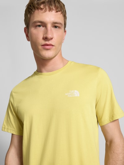 Mannelijk model draagt T-shirt met Labelprint van The North Face in lichtgeel, katoenmix, regular fit, ronde hals, detailopname bovenlichaam.