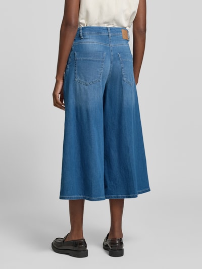 Frauenmodel trägt Wide Fit Jeans in verkürzter Passform Modell 'Ella' von MAC, blauer elastischer Baumwoll-Mix, Gesäßtaschen, Ganzkörperansicht Rückansicht.