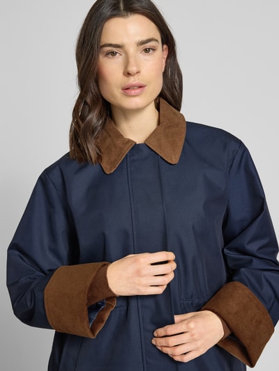 Frauenmodel trägt Parka mit Umlegekragen und Eingrifftaschen Modell 'ANCA' von YAS aus Baumwoll-Mix in Regular-Fit, Nahaufnahme Oberkörper. Rückenlänge Größe 36: 72 cm, Schulterbreite: 45 cm, Brustweite: 53 cm, Ärmellänge: 61 cm. Farbe: Dunkelblau mit braunen Details, glatte und strukturierte Texturen.