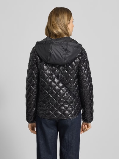 Frauenmodel trägt schwarze Regular Fit Jacke in Stepp-Optik Modell 'YOSIE' von Frieda & Freddies, Kapuze, Ganzkörperansicht Rückansicht.