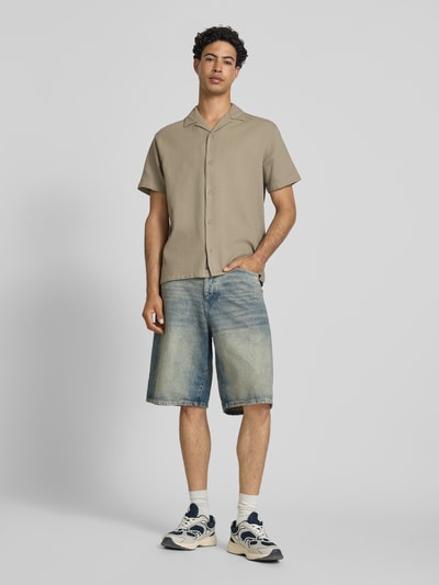 Męski model nosi koszulę casualową z bawełny o kroju regular fit Jack & Jones, model 'Global', fakturowany wzór, krótki rękaw, kołnierz z połami, listwa guzikowa, długość tyłu w rozmiarze M: 71 cm, szerokość ramion w rozmiarze M: 51 cm, długość rękawów w rozmiarze M: 25 cm, jednolity beżowy kolor, gładka tekstura, widok całej sylwetki z przodu.