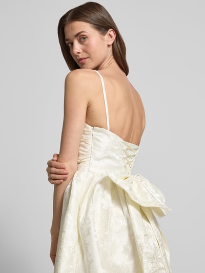 Frauenmodel trägt Minikleid mit floralem Allover-Stitching von Hey Kyla in Creme, Zierschleife, abnehmbare Träger, Rückenlänge 85 cm, taillierte Passform, Ganzkörperansicht Rückansicht.