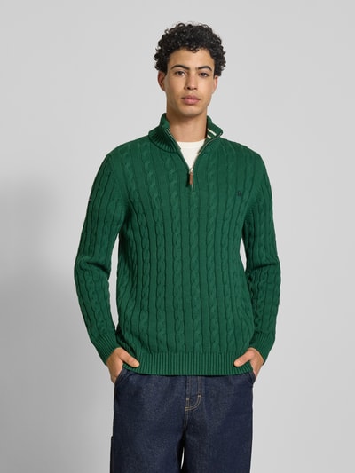 Mannenmodel draagt gebreide pullover uit puur katoen met schipperskraag, kabelpatroon en labeldetail van Superdry, groene kleur, pasvorm eng, ribboorden, ruglengte maat M 70 cm, mouwlengte maat M 71 cm, voorkant volledige lichaamsopname.