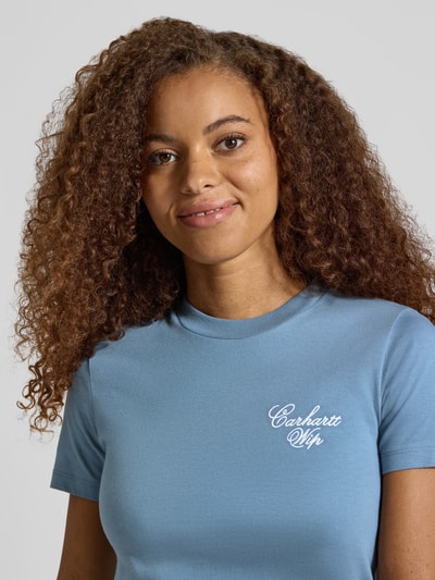 Frauenmodel trägt Slim Fit T-Shirt aus reiner Baumwolle Modell 'Gracious' von Carhartt Work In Progress in Hellblau, Nahaufnahme Oberkörper. Rundhalsausschnitt, Label-Print, Rückenlänge bei Größe S 53 cm.