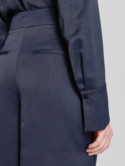 Kobieta nosi Wide Fit Stoffhose mit Strukturmuster od Christian Berg Cocktail, granatowy kolor, tkanina o kwiatowej strukturze, szeroki krój, zaszewki, szczegółowe ujęcie tyłu pasa i kieszeni, zapięcie na haftkę i zamek, Szerokość w rozmiarze 36: 40 cm, długość wewnętrzna nogawki: 80 cm, zbliżenie tylnej części pasa.