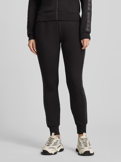 Frauenmodel trägt schwarze Sweatpants mit elastischem Bund Modell 'ALLIE' von Guess Activewear, lockerer Schnitt, Nahaufnahme Unterkörper.