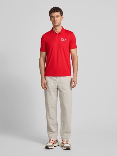 Männermodel trägt Regular Fit Poloshirt mit Logo von EA7 Emporio Armani in Rot, glatter Stoff, Knopfleiste, Logo vorne, Ganzkörperansicht von vorne