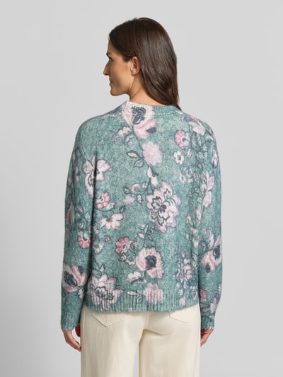 Vrouwenmodel draagt Relaxed Fit Strickpullover mit Leinen-Anteil van Christian Berg Woman in groen met bloemenprint, elastische materiaalmix met linnen, ribboorden, bies, lange mouw, ruglengte bij maat S 57 cm, mouwlengte bij maat S 62 cm, geheel zicht van achteren.