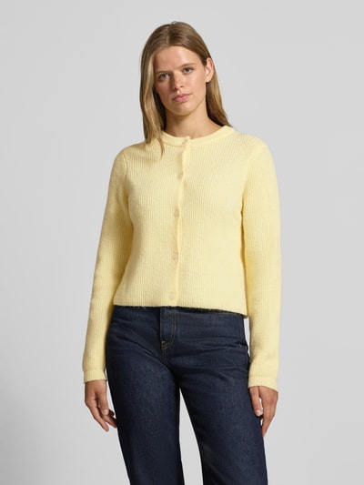 Frauenmodel trägt Strickjacke mit Woll-Anteil Modell 'SILLY' von PIECES in hellgelb mit grober Struktur, kombiniert zu dunkler Jeans, Ganzkörperansicht von vorne.