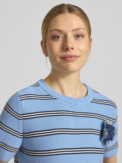 Vrouwenmodel draagt Strickshirt met florale applicatie van Oui, lichtblauw met zwarte-witte strepen, pure katoen, regular fit, ronde hals, detailopname bovenlichaam.