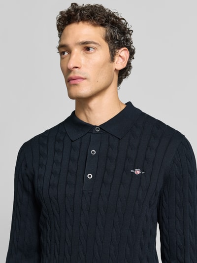 Männermodel trägt Regular Fit Pullover aus reiner Baumwolle von GANT in Dunkelblau mit Strickmuster und Logo, Nahaufnahme Oberkörper.
