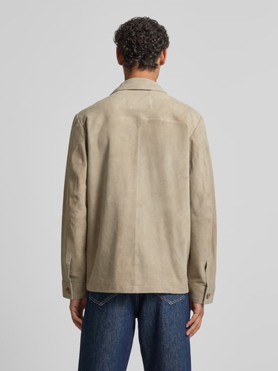 Mannenmodel draagt Regular Fit Ziegenlederjacke mit Brusttasche van Marc O'Polo in wildleerlook, echte geitenleer, platte kraag, knoopsluiting, borstzak, zijsteekzakken, lange mouw, labelapplicatie, kleur beige, materiaalverwerking velours. Ganzkörperansicht Rückansicht.