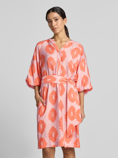 Frauenmodel trägt Knielanges Kleid aus Viskose-Mix von Christian Berg Woman in Rosa und Orange mit Taillenband, Serafino-Ausschnitt, lockerer Passform, Halbarm, Knopfleiste, Ganzkörperansicht von vorne.