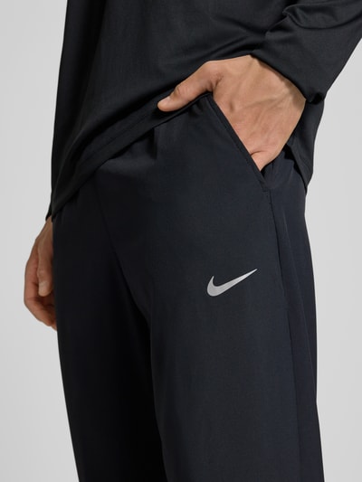 Mężczyzna nosi Form Pants mit Logo-Print und Eingrifftaschen von NIKE TRAINING, czarne, dopasowany krój, elastyczny pas, wpuszczane kieszenie, nadruk z logo, elastyczne wykończenia, długość wewnętrzna nogawki w rozmiarze M: 38 cm, zbliżenie na kieszeń i logo, detal