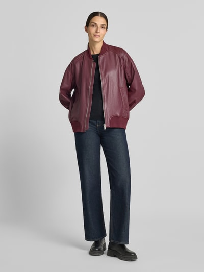 Frauenmodel trägt Regular Fit Bomberjacke aus reinem Schafsleder Modell 'Ruby' von MOS MOSH in Dunkelrot, glatte Textur, Stehkragen, Eingrifftaschen, Reißverschluss, elastische Abschlüsse, Ganzkörperansicht von vorne.