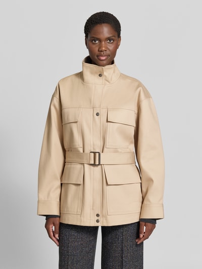 Frauenmodel trägt Funktionsjacke mit Taillengürtel Modell 'ODIN' von Anine Bing in Beige, matte Webware, aufgesetzte Taschen, Ganzkörperansicht von vorne.