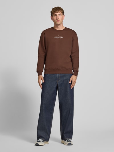 Männermodel trägt Regular Fit Sweatshirt aus Baumwoll-Mix mit Label-Detail von Alpha Industries in Braun, elastische Abschlüsse, Ganzkörperansicht von vorne. Rückenlänge bei Größe M: 67 cm, Ärmellänge bei Größe M: 63 cm.