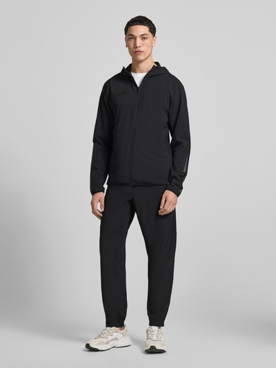 Męskimodel nosi Slim Fit Funktionsjacke aus schnelltrocknendem Material von adidas Sportswear, efekt: jednolity kolor, krój slim fit, kaptur, zamek błyskawiczny, nadruk z logo, długi rękaw, szybkoschnący, z regulacją wilgoci, boczne kieszenie zapinane na zamek błyskawiczny; Ganzkörperansicht von vorne.