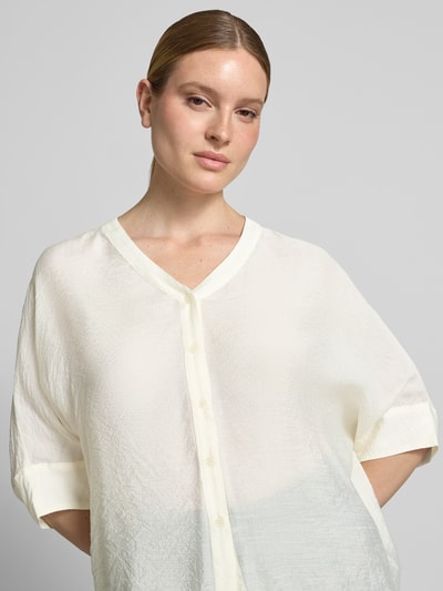 Modelka nosi Relaxed Fit Bluse aus Viskose-Mix mit 3/4-Arm von comma, kolor kremowy, dekolt w serek, listwa guzikowa, mieszanka wiskozy, krój relaxed fit, długość tyłu w rozmiarze S: 62 cm, długość rękawów w rozmiarze S: 18 cm, zbliżenie na górną część ciała.