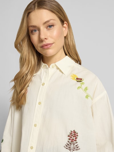 Frauenmodel trägt Relaxed Fit Bluse mit Stitchings von Scotch & Soda aus Baumwoll-Leinen-Mix, Naturfarben, floral bestickt, Nahaufnahme Oberkörper.