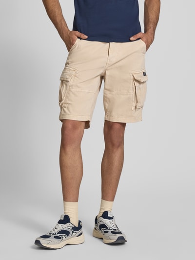 Männermodel trägt Straight Fit Shorts mit Cargo-Taschen Modell 'Core' von Superdry im Beige-Ton, Baumwoll-Mix, Ganzkörperansicht von vorne. Bundweite 42 cm, Innenbeinlänge 23 cm, Knopf- und Reißverschluss, Eingriffstaschen und Gesäßtaschen.