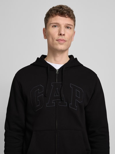 Mannelijk model draagt Sweatjacke mit getrennter Kängurutasche van GAP in zwart, katoenmix, loose fit, label-stitching, elastische boorden, detailopname bovenlichaam.