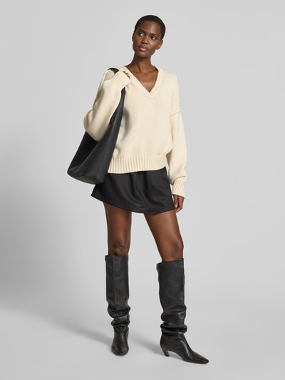Frauenmodel trägt Oversized Pullover in Strick-Optik von black palms aus Baumwoll-Mix, V-Ausschnitt, elastische Abschlüsse, cremefarben, Ganzkörperansicht von vorne.