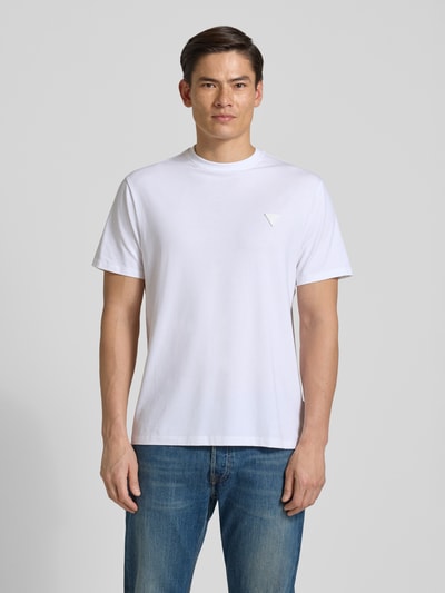 Männermodel trägt T-Shirt mit Logo und Rundhalsausschnitt von Guess, weiß, Baumwoll-Mix mit Modal-Anteil, Relaxed Fit, Ganzkörperansicht von vorne.