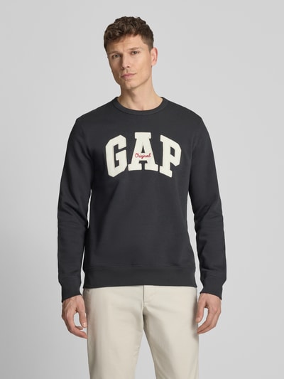 Mannenmodel draagt Sweatshirt mit Logo und Rundhalsausschnitt van GAP in zwart, katoenmix, regular fit, logoprint, ronde hals, ruglengte maat M 69 cm, mouwlengte 65 cm, vooraanzicht, bovenlichaam close-up.