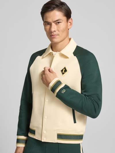 Männermodel trägt Regular Fit Sweatjacke aus Baumwoll-Mix von Lacoste in Creme und Dunkelgrün mit Logo-Details, Nahaufnahme Oberkörper. Herren Sweatjacke von Lacoste