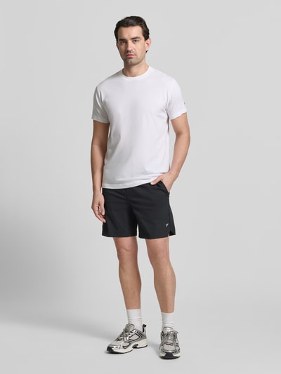 Männermodel trägt Regular Fit Shorts mit Logo-Print von Fabletics, elastischer Material-Mix, schwarzer Farbton, Ganzkörperansicht von vorne.
