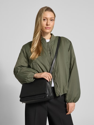 Kobiece model prezentuje Crossbody Bag mit Logo-Prägung Modell 'Hera' od LIEBESKIND BERLIN, czarny, z przetłoczeniem logo, smukły pasek na ramię, zamknięcie na zamek, szerokość w rozmiarze 1: 24 cm, długość w rozmiarze 1: 18 cm, głębokość w rozmiarze 1: 13 cm, długość paska w rozmiarze 1: 123 cm, widok na górną część ciała z przodu