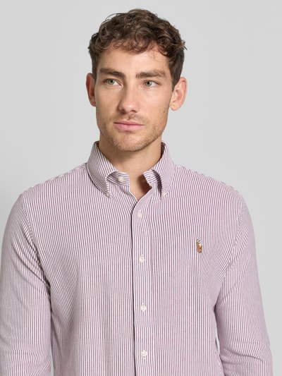 Męski model nosi Freizeithemd mit Knopfleiste od Polo Ralph Lauren, bawełna, krój regular fit, kołnierzyk button-down, label-stitching, zapięcie na guziki, długość tyłu w rozmiarze M: 76 cm, szerokość w rozmiarze M: 46 cm, długość rękawa w rozmiarze M: 67 cm, cienkie bordowo-białe paski, gładka faktura, widok na górną część ciała z przodu