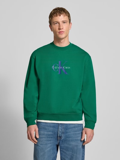Männermodel trägt Sweatshirt mit Rundhalsausschnitt und Logo von Calvin Klein Jeans, grün, Reine Baumwolle, Regular-Fit, Ganzkörperansicht von vorne.