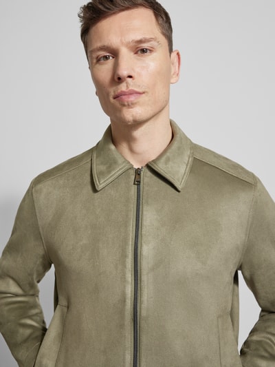 Mężczyznamodel nosi Regular Fit Jacke in Lederoptik od Tom Tailor Denim, efekt: jednolity kolor, imitacja skóry, wykładany kołnierz, zamek błyskawiczny, długi rękaw, proste zakończenia, wpuszczane kieszenie boczne, kieszeń wewnętrzna, wykończenie materiału: sztuczna skóra, jasna oliwkowa faktura, gładka powierzchnia, Nahaufnahme górnej części ciała.