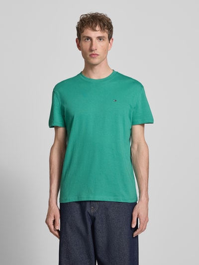 Männermodel trägt Regular Fit T-Shirt aus reiner Baumwolle von Tommy Jeans in Grün, unifarben, Logo-Stitching, Ganzkörperansicht von vorne.